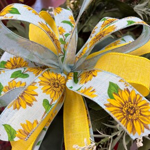 May include: A decorative bow made of layered fabric ribbons. The design features a light blue ribbon with a yellow sunflower and green leaf print, paired with solid bright yellow and dark green ribbons, all arranged in multiple loops.
