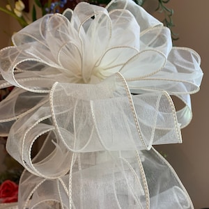 May include: A white sheer ribbon bow with a white satin edge. The bow is tied in a large, full shape and is perfect for adding a touch of elegance to any gift or decor.
