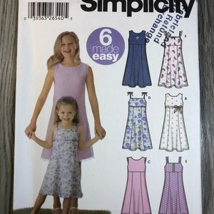 May include: Simplicity sewing pattern number 5641 for girls' dresses. The pattern includes six different styles, including a blue dress with a white flower, a white dress with pink flowers, a purple dress with white polka dots, a pink dress with white trim, a purple dress with white flowers, and a white dress with blue flowers. The pattern is labeled "6 made easy".
