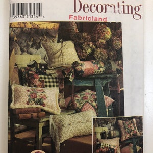 Puede incluir: Un patrón de costura Simplicity Home Decorating para almohadas, que presenta una variedad de diseños y colores. El patrón incluye instrucciones para hacer almohadas con patrones florales, a cuadros y geométricos. El patrón está etiquetado como "Simplicity Home Decorating" y "Fabricland".