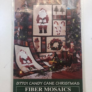 May include: A Christmas-themed cross-stitch pattern featuring Santa Claus, candy canes, a wreath, and a Christmas tree. The pattern is titled "87701 Candy Cane Christmas" and is from Fiber Mosaics.