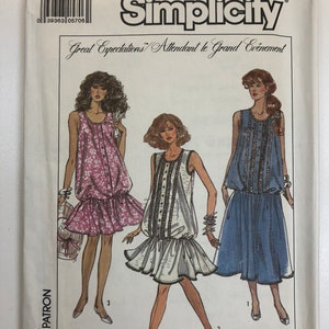 Puede incluir: Patrón de costura Simplicity 8701 para las tallas 10-12-14. El patrón presenta tres estilos diferentes de vestidos: un vestido de estampado floral, un vestido blanco con ribetes negros y un vestido azul con ribetes plateados. El patrón se titula "Great Expectations" y "Attendant le Grand Evénement".
