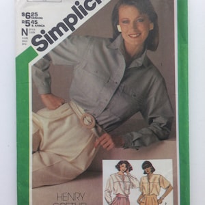 May include: Simplicity sewing pattern with a woman in a grey shirt and cream trousers. The pattern includes designs by Henry Grethel. The package is green and white with the Simplicity logo.