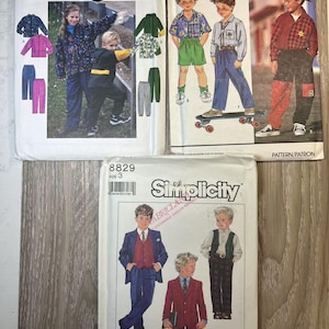 Puede incluir: Tres patrones de costura Simplicity para ropa de niño. Los patrones son para una chaqueta y un pantalón, una camisa y pantalones cortos, y un traje. Los patrones están todos en papel blanco con texto negro e ilustraciones.