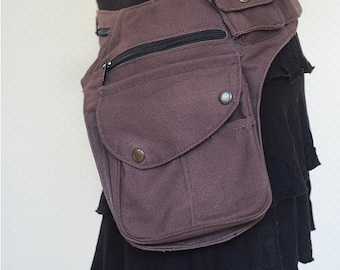 May include: Brown hip bag with multiple pockets and a zipper closure. The bag is made of a brown fabric and has a black zipper. The word "Brown" is written in cursive in the upper right corner. The bag is worn over a black skirt.