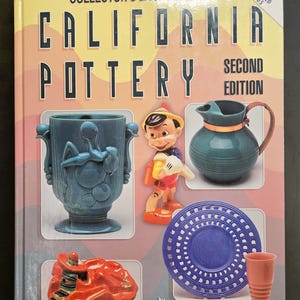 May include: A book titled "Collector's Encyclopedia California Pottery Second Edition" with images of various pottery pieces. Featured items include a blue vase, a Pinocchio figurine, a teal pitcher, a red sculpture, a blue plate, and a pink cup.