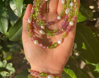 Könnte beinhalten: Ein mehrreihiges Halsketten- und Armbandset aus grünen und rosafarbenen Edelsteinperlen und weißen Perlen. Halskette und Armband sind auf einer goldenen Kette aufgefädelt.