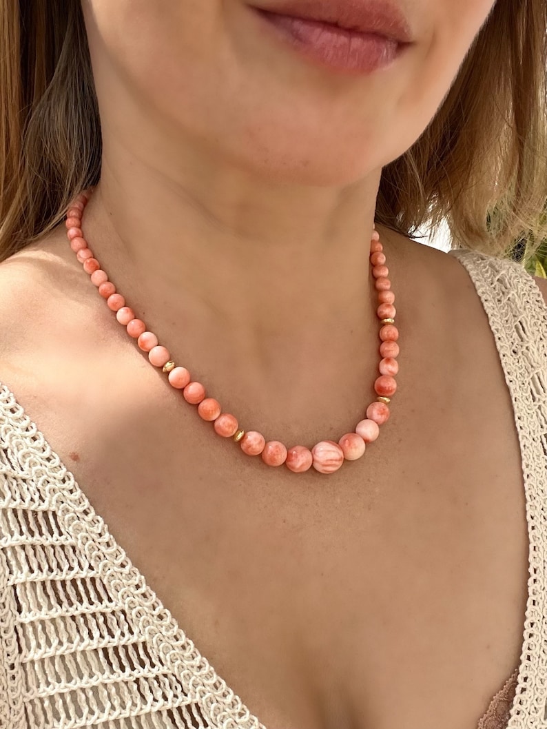 May include: A delicate necklace made of pink coral beads with gold accents. The necklace is made of natural coral and is a beautiful and unique piece of jewelry.