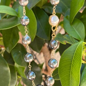 May include: A gold chain necklace with black and white pearls. The necklace has a clasp with a single white pearl.