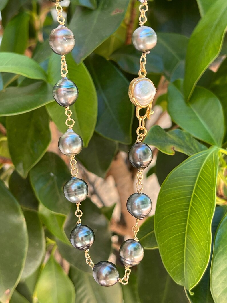 May include: A gold chain necklace with black and white pearls. The necklace has a clasp with a single white pearl.