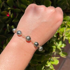 May include: A bracelet with a gold chain and dark gray pearls.