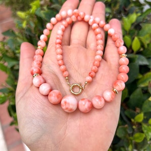 May include: A pink coral necklace with gold accents. The necklace is made of round beads and has a clasp closure.