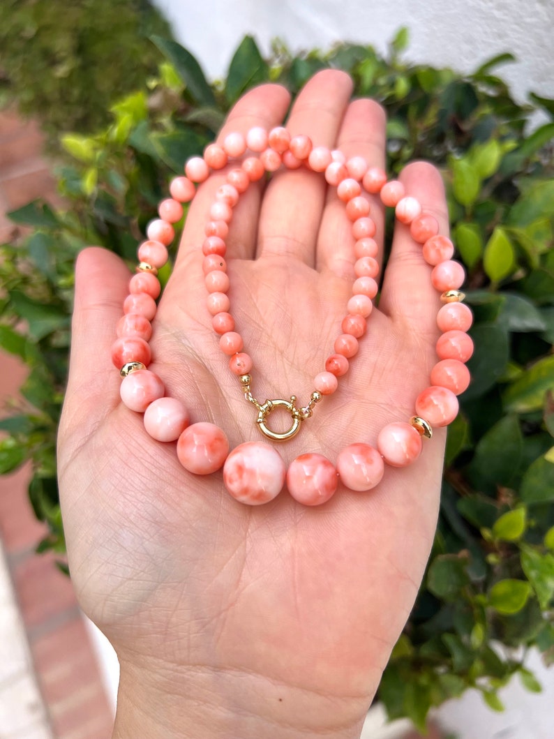 May include: A pink coral necklace with gold accents. The necklace is made of round beads and has a clasp closure.