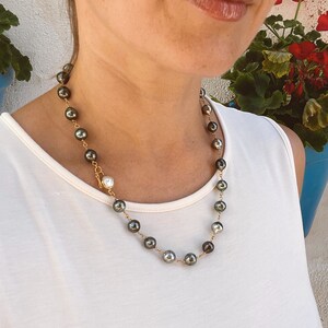 May include: A gold chain necklace with dark green and white pearls. The necklace is worn by a person with a white tank top.