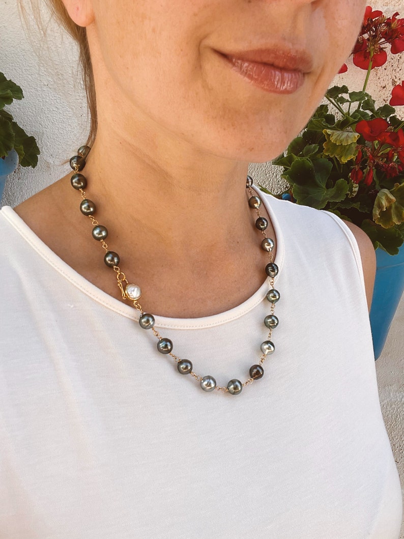 May include: A gold chain necklace with dark green and white pearls. The necklace is worn by a person with a white tank top.