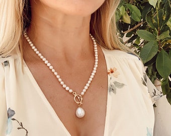May include: A delicate pearl necklace with a large, teardrop-shaped pearl pendant. The necklace is made of small, white pearls and has a gold clasp.