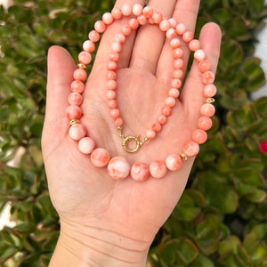 May include: A pink coral necklace with gold beads and a gold clasp. The necklace is made of round coral beads and is approximately 18 inches long.