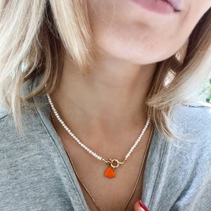 May include: A white pearl necklace with a gold clasp and a small orange heart charm.