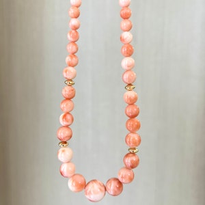 May include: A necklace made of pink coral beads with gold accents. The beads are round and have a smooth, polished finish.