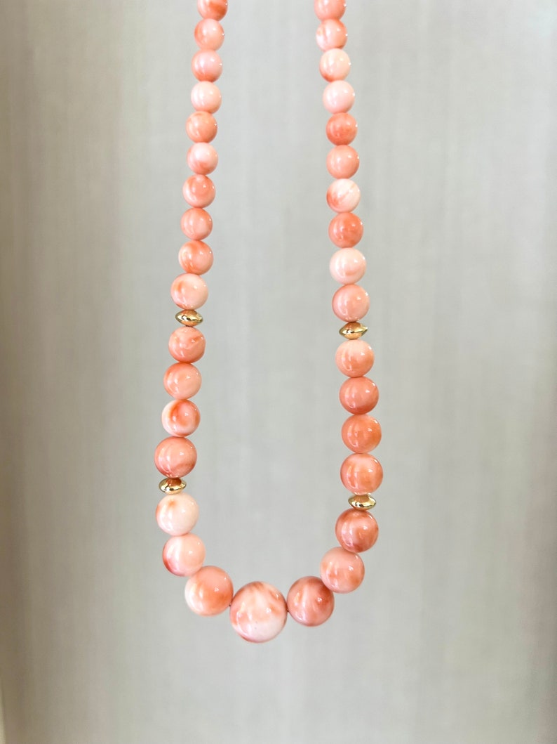 May include: A necklace made of pink coral beads with gold accents. The beads are round and have a smooth, polished finish.