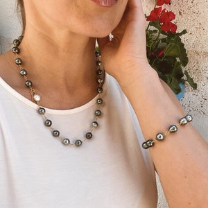 May include: A black pearl necklace and bracelet set with a gold chain. The necklace has a single white pearl pendant.