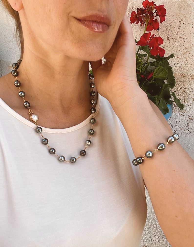 May include: A black pearl necklace and bracelet set with a gold chain. The necklace has a single white pearl pendant.