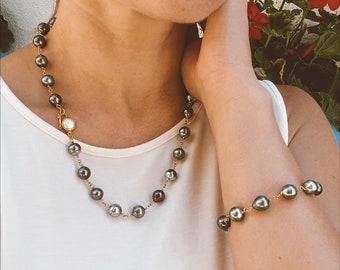 Op de afbeelding: Een set zwarte en groene parelsieraden met een ketting en een armband. De ketting heeft een enkele witte parel accent.