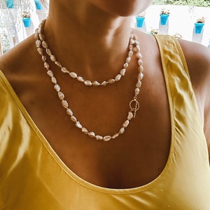 May include: A double strand pearl necklace with a gold clasp. The necklace is made of white pearls and has a simple design.