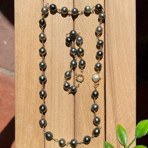 May include: A black and gold pearl necklace with a white pearl clasp. The necklace is made of round pearls and is strung on a gold chain.