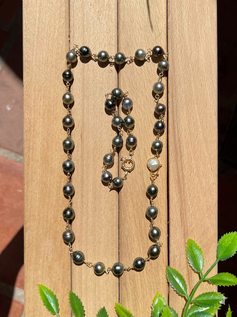 May include: A black and gold pearl necklace with a white pearl clasp. The necklace is made of round pearls and is strung on a gold chain.