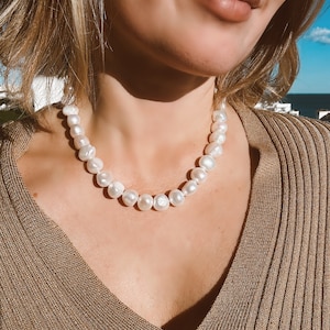 Pode incluir: Um colar de pérolas brancas com um design simples. As pérolas são redondas e lisas, e o colar é feito de uma corrente delicada.