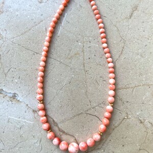 May include: A pink coral necklace with gold accents. The necklace is made of round beads and has a clasp closure.