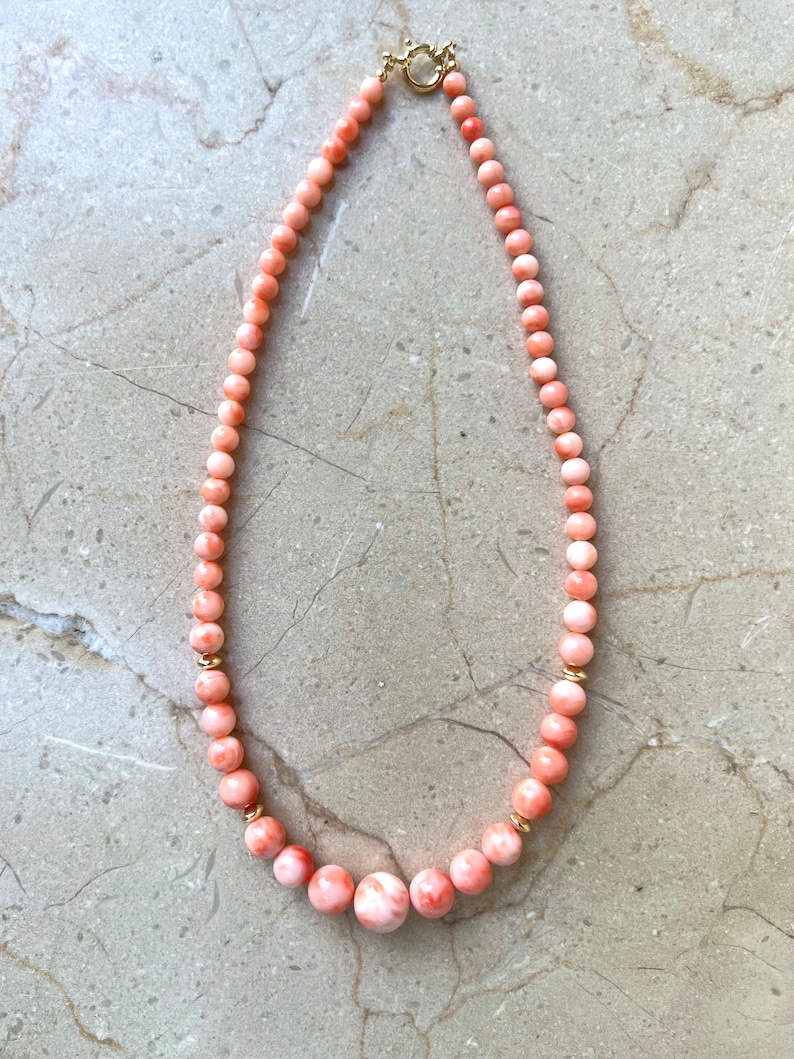 May include: A pink coral necklace with gold accents. The necklace is made of round beads and has a clasp closure.
