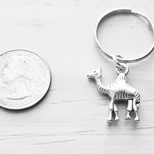 May include: A silver camel keychain with a silver key ring. The keychain is about the size of a US quarter.