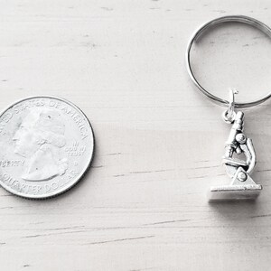 May include: Silver microscope keychain with a silver key ring. The keychain is about the size of a US quarter.