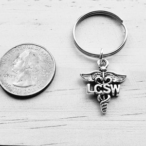 May include: Silver keychain with a caduceus symbol and the letters LCSW.