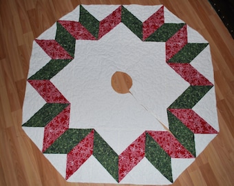 May include: A white quilted Christmas tree skirt with a green and red snowflake patterned border. The skirt has a center opening for the tree trunk.