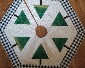 May include: A white quilted Christmas tree skirt with a black and white checkered border. The skirt features six green felt Christmas trees with brown trunks.