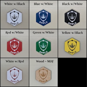 Op de afbeelding: Een set van zeshoekige houten onderzetters met een schildontwerp. De onderzetters zijn verkrijgbaar in verschillende kleuren, waaronder wit, zwart, blauw, rood, groen, geel en hout.