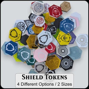 May include: A collection of hexagonal tokens in various colors including red, blue, yellow, black, and metallic finishes. Each token features a shield icon and the word SHIELD printed on the surface. A label below reads SHIELD TOKENS 4 Different Options / 2 Sizes.