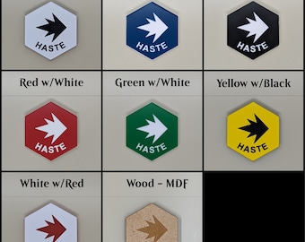 May include: Set of 8 hexagonal game tokens with the word "HASTE" printed on each. The tokens are in various colors, including white, black, blue, red, green, yellow, and wood.