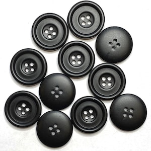 May include: Ten black plastic buttons with four holes each. The buttons are arranged in a loose circle on a white background.