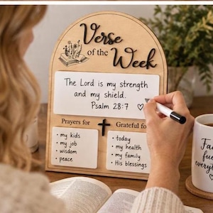 May include: An arched wooden display board titled Verse of the Week with a white dry-erase surface. It features sections for prayers and gratitude, including text like The Lord is my strength and my shield. Psalm 28:7 and lists for kids and health.