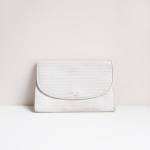Könnte beinhalten: Eine weiße Clutch mit einem strukturierten, gestreiften Design. Die Clutch hat einen abgerundeten Klappenverschluss.