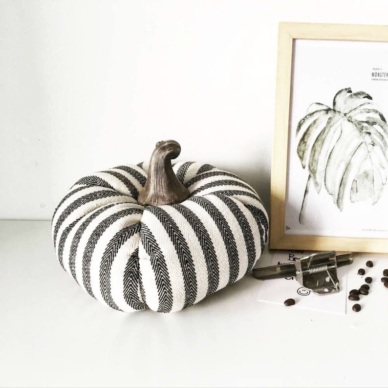 May include: A black and white striped fabric pumpkin with a brown wooden stem. The pumpkin is sitting on a white surface.