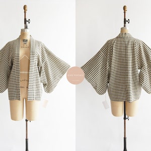 Può includere: Un kimono bianco e nero a quadri con maniche lunghe. Il kimono è esposto su un manichino.