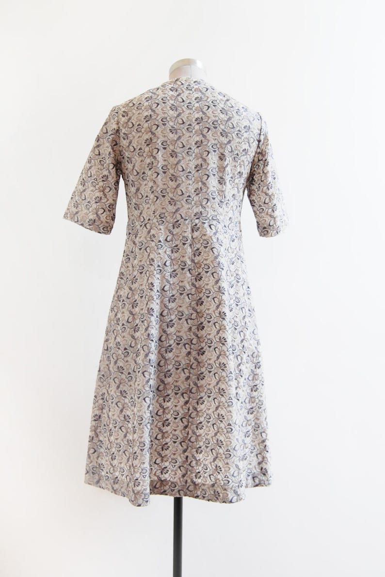May include: A white dress with a black floral pattern. The dress has a round neckline and short sleeves. It is fitted at the waist and flares out to the hem.