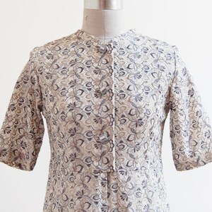 May include: A beige dress with a floral pattern and silver buttons. The dress has a short sleeve and a fitted bodice.