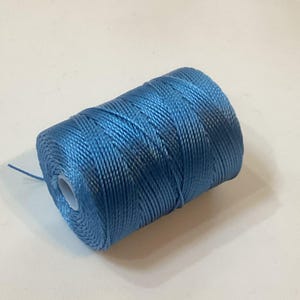 May include: A spool of bright blue nylon thread. The thread is tightly wound around a white cardboard core. The color is a vibrant, solid blue, and the thread has a slight sheen. This thread is suitable for various crafting projects.