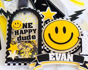 May include: A black and white checkered banner with the text "Evan is one" and a yellow smiley face. There is a yellow smiley face on a black and white checkered background with the text "One Happy Dude" in a clear plastic frame. There is a yellow smiley face on a black and white checkered background with the text "Evan" in a yellow banner.